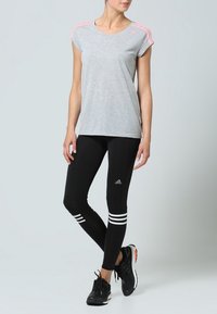 Grå atletisk t-shirt med rosa detaljer, i kombination med svarta leggings som har tre vita ränder vid anklarna. Svarta träningsskor fulländar looken.