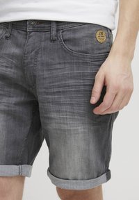 Grå denimshorts med en lett falming, rullekanter, femlommers design og et merket lap på fronten av linningen.