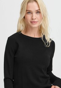 Maglione nero a maniche lunghe in un design aderente con collo e polsini a costine, realizzato in un tessuto morbido e leggero.