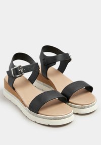 Czarne skórzane sandały z dwoma szerokimi paskami, regulowanym paskiem wokół kostki i lekko drewnopodobną podeszwą na koturnie z metalicznym akcentem w kolorze srebrnym.