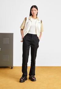 Short-sleeved shirt in white and light brown, paired with black trousers and chunky black sandals with circular hardware accents.