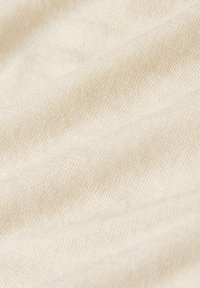 Close-up van beige gebreide stof met zichtbaar weefpatroon en zachte plooien.