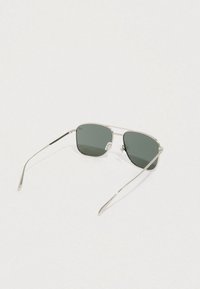 Gafas de sol con montura metálica plateada, lentes tintadas en verde, forma cuadrada y varillas delgadas y elegantes. Almohadillas nasales transparentes destacadas para mayor comodidad.
