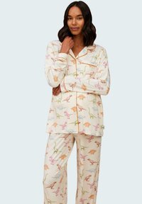Dynamiskt tvådelat pyjamas-set i mjukt tyg, med en krämfärgad bakgrund och färgglada dinosaurie-mönster. Inkluderar en knäpp-topp och byxor.