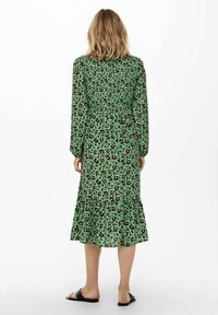 Grünes Leopardenmuster-Kleid mit langen Ärmeln, gerafftem Taillenbereich und einem rüschierten Saum. Der Stoff ist leicht und hat eine glatte Textur.