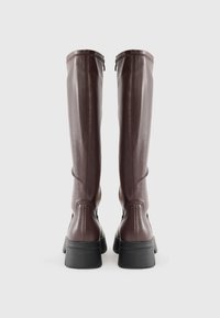 Bottes en cuir marron à hauteur de genou avec une texture lisse, dotées d'un bout rond et d'une semelle noire épaisse. Détail de fermeture éclair sur le côté.