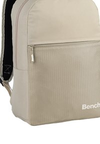 Beige backpack with a textured front pocket, featuring a hexagonal pattern. Includes a zipper closure and "Bench" logo in white.