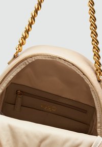 Borsa rotonda beige con finitura lucida, tracolla in catena dorata e interno con zip che include una piccola tasca con zip.