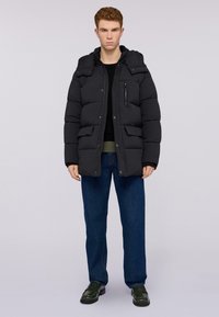 Svart puffjacka med huva, med en zip-försedd bröstficka, två framfickor och quiltad design. Bärs med mörka jeans och en svart topp.