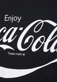 Černé tričko s bílým nápisem "Enjoy Coca-Cola" a ochrannou známkou, doplněné stylizovanou bílou vlnou.