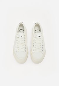 Vit kanvas sneakers med platta snörningar, gummisålar och texturerade sidopaneler. Logotyp synlig på tungan. Enkel, lågprofil design.