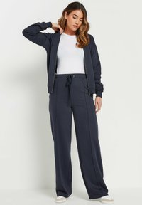 Navy blauwe zip-up sweatshirt met geribbelde manchetten, gecombineerd met bijpassende wijdvallende sweatpants met een trekkoord in de taille en zijnaad.