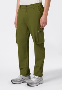 Olivgrüne Cargo-Hosen mit geradem Schnitt, Reißverschlusstasche an der Seite und Gürtelschlaufen, aus leichtem Material gefertigt. Kombiniert mit grauen Sportschuhen.