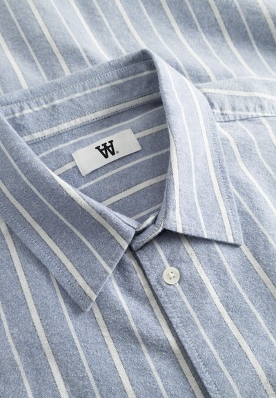 Chemise en coton de couleur bleu clair avec des rayures verticales blanches, col boutonné, et une petite étiquette portant un "W" près du col.