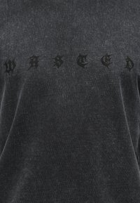 Σκούρο γκρι ύφασμα με τη λέξη «WASTED» τυπωμένη σε μαύρα γράμματα γοτθικού στιλ.