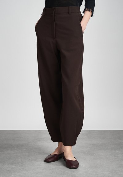 Pantalon taille haute marron avec une coupe ample, des plis marqués, des poches latérales et une texture lisse. Associé à des ballerines bordeaux.
