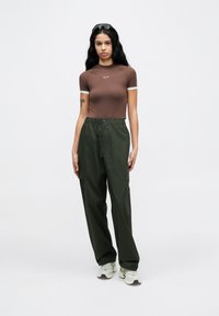Καφέ εφαρμοστό κοντομάνικο τοπ με λευκές λεπτομέρειες, συνδυασμένο με χαλαρά χακί παντελόνια cargo και λευκά αθλητικά παπούτσια.