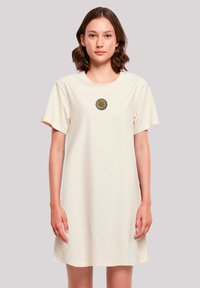 Crème-kleurige katoenen t-shirt jurk met korte mouwen en een ronde hals, voorzien van een geborduurd madeliefje op de borst.