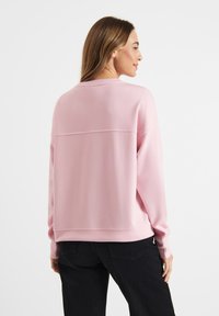 Light pink sweatshirt featuring a crew neck, long sleeves, and a relaxed fit. Smooth texture with a horizontal seam detail across the back.