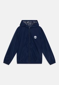 Navy blue lightweight jacket with a hood, front zipper, elastic cuffs, and a white tree logo on the left chest. Smooth texture, casual design.