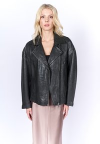 Giacca da motociclista in pelle nera con finitura testurizzata, colletto a punte e zip asimmetrica, abbinata a una gonna in satin rosa chiaro.