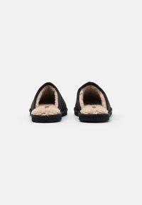 Pantofi slip-on negri cu o căptușeală moale din blană bej. Au un design simplu, vârful rotunjit și talpa plată din cauciuc. Detalii hardware minime.
