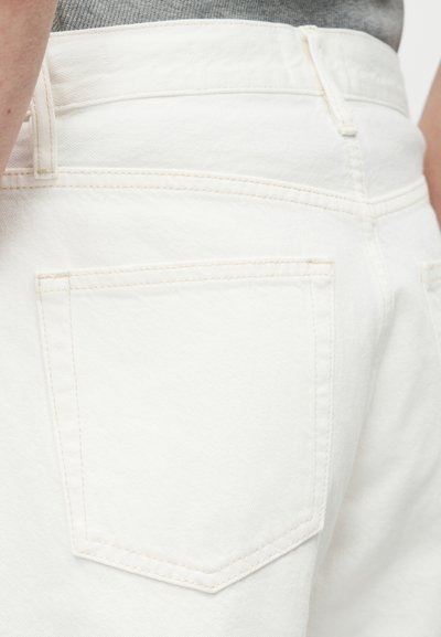Κλείσιμο πλάνου ενός ατόμου που φοράει λευκό τζιν παντελόνι με λεπτομέρεια πίσω τσέπης και μερικό μέρος γκρι πουκαμίσου ορατό πάνω από τη ζώνη.