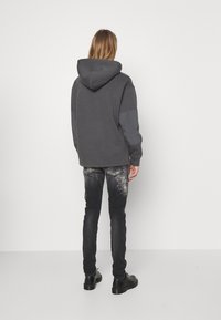 Sudadera gris con capucha y corte relajado, combinada con unos jeans negros de diseño moteado. El conjunto se completa con unos zapatos negros.