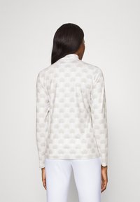 Långärmad topp i ljus krämfärg med ett upphöjt skalmönster. Mjukt material med standardkrage och figurnära passform, som slutar vid höften.