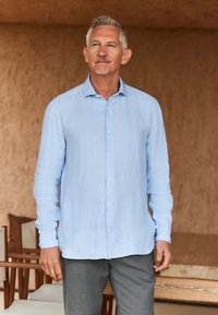 Lichtblauw linnen overhemd met een knoopsluiting aan de kraag, lange mouwen en een comfortabele, losse pasvorm, gecombineerd met grijze broek. Zachte textuur en casual ontwerp.