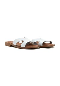 Sandales blanches en cuir avec une conception à bandeau divisé et une semelle plate marron. Présente des détails découpés sur le dessus.