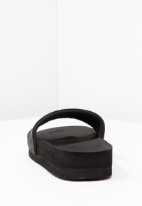 Black slide sandal featuring a textured upper strap and a flat, cushioned sole. The design is minimalistic with a seamless profile.