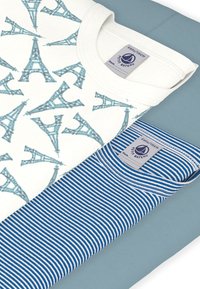 Deux t-shirts : l'un blanc avec un motif de la tour Eiffel en sarcelle ; l'autre à rayures bleues et blanches. Les deux comportent une étiquette avec la marque "Petit Bateau".