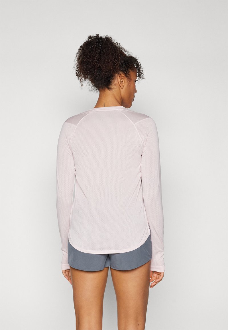 Langärmliges Sportshirt in Hellrosa, hergestellt aus strukturiertem Stoff, mit Raglanärmeln und seitlichen Schlitzen. Kombiniert mit grauen Sportshorts.