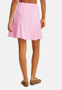 Ružová rozšírená sukňa s hladkou textúrou, ktorá sedí na páse. V kombinácii s plochými topánkami s leopardím vzorom a malými zlatými akcentmi.