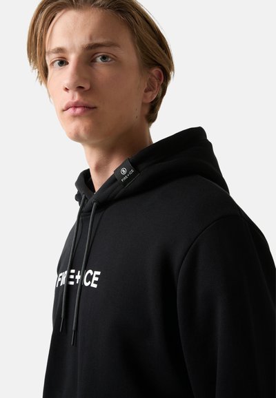 Jonge man met licht haar in een zwarte hoodie met witte "FIRE + ICE" tekst en een capuchonlabel, lichtjes naar links kijkend op een witte achtergrond.