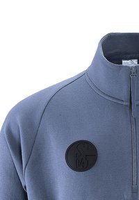 Felpa con zip in tessuto blu chiaro testurizzato, dotata di una toppa circolare nera con scritte in rilievo nella zona sinistra del petto.