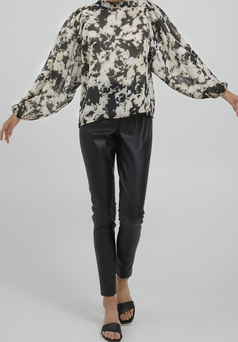 Blusa floreale in bianco e nero con maniche lunghe e a sbuffo, abbinata a pantaloni fitted in ecopelle nera e sandali neri a scivolo.