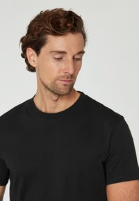 Svart bomullströja med rund halsringning och korta ärmar, med en subtil "Sail Racing"-logotyp i präglad tryck på bröstet.