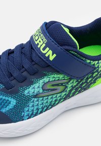 Skechers GOrun shoes featuring a navy upper with green and blue patterned accents, a secure strap, and a cushioned white sole.