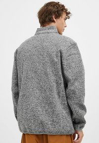 Pulover gri din fleece cu guler înalt, material texturat, mâneci largi și o croială relaxată, având un tiv și manșete elastice.