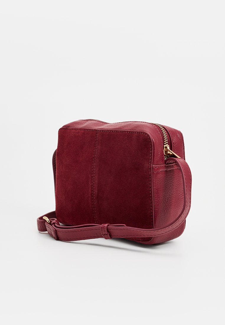 Bordowa skórzana torba z zamszem i teksturowanym wykończeniem, prostokątna forma, zamek błyskawiczny oraz regulowany pasek. Gładkie i miękkie faktury.