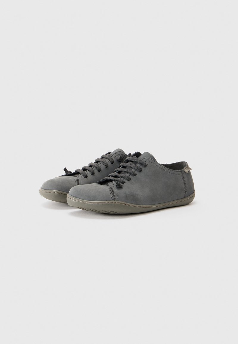 Un paio di scarpe casual grigie scure con lacci, punte arrotondate e suole in gomma flessibili su sfondo bianco.