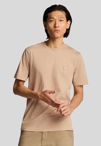 T-shirt di cotone beige chiaro con maniche corte e colletto tondo, con un piccolo logo ricamato sul petto. Tessuto liscio.