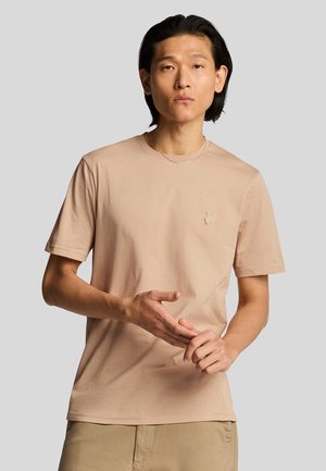 Ljusbeige bomullströja med korta ärmar och rund hals, med en liten broderad logotyp på bröstet. Slät struktur.