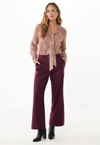 Blusa rosa chiaro con un motivo geometrico, legata al collo; abbinata a pantaloni larghi bordeaux e stivaletti neri.