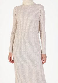Robe tricotée en beige clair avec une texture en côtes verticales. Manches longues, décolleté rond et motifs de cœurs subtils partout.