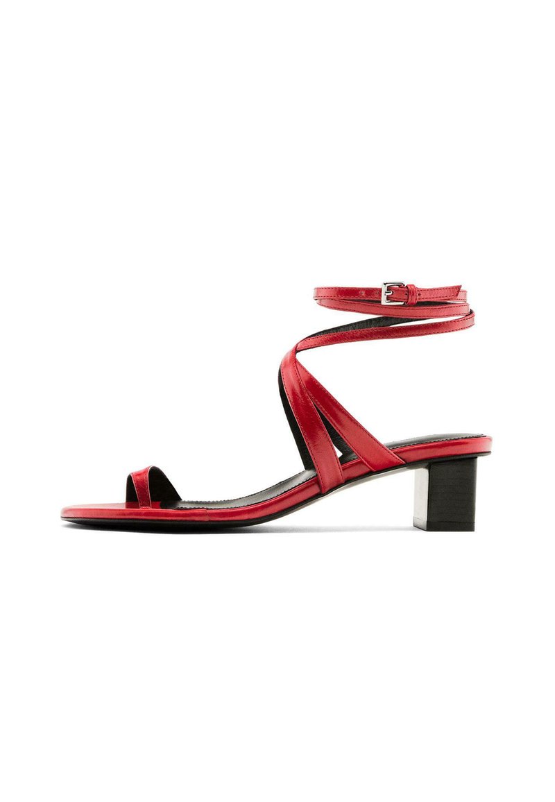 Sandale rouge à lanières avec un talon block, présentant une finition brillante, un design à bout ouvert et des brides de cheville étroites fixées par une boucle.