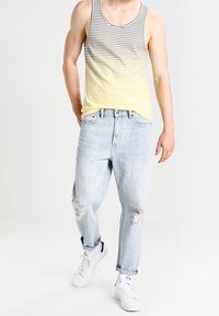 Top de tirantes a rayas que va del gris al amarillo, combinado con jeans claros despeinados y zapatillas blancas. Conjunto sencillo y casual.