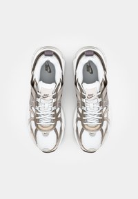 Nike-tenniskenkä, jossa on valkoinen verkko-yläosa, beige ja harmaita yksityiskohtia, teksturoitu pohja ja tasaiset nauhat. Logo näkyy kielellä.